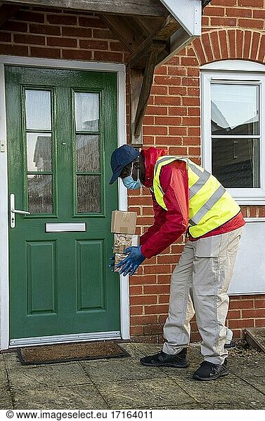Männlicher Kurier  der während der Covid-19-Epidemie Pakete und Päckchen ausliefert und dabei Handschuhe und einen Mundschutz trägt  Hampshire  England  Vereinigtes Königreich.