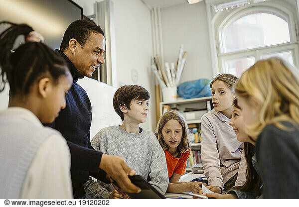 Männlicher Lehrer teilt sich einen Tablet-PC mit Schülern  die im Klassenzimmer diskutieren