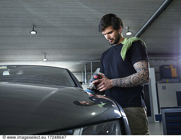 Männlicher Mechaniker poliert in einer Werkstatt die Motorhaube eines Autos