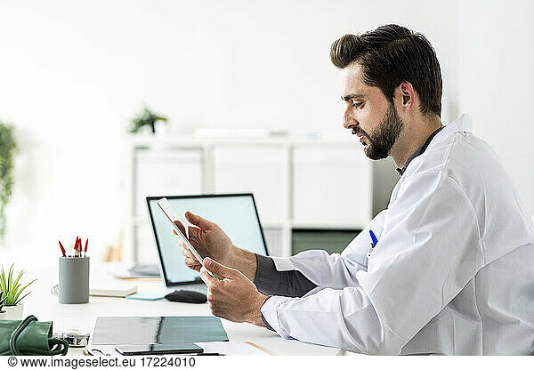 Männlicher Mitarbeiter im Gesundheitswesen  der am Schreibtisch sitzend ein digitales Tablet benutzt