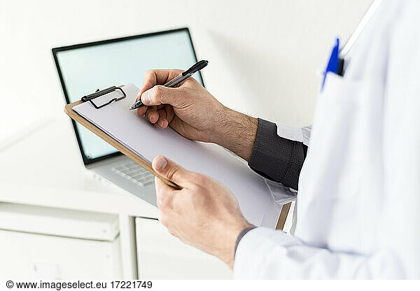Männlicher Mitarbeiter im Gesundheitswesen hält ein Klemmbrett und schreibt auf Papier