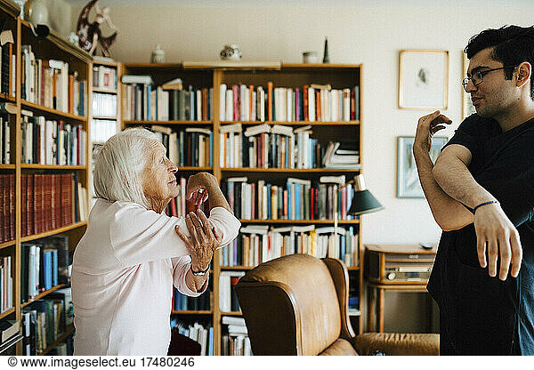 Männlicher Mitarbeiter im Gesundheitswesen hilft einer älteren Frau bei ihren Übungen zu Hause