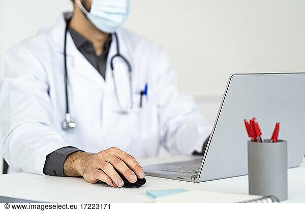 Männlicher Mitarbeiter im Gesundheitswesen mit Schutzmaske und Laptop