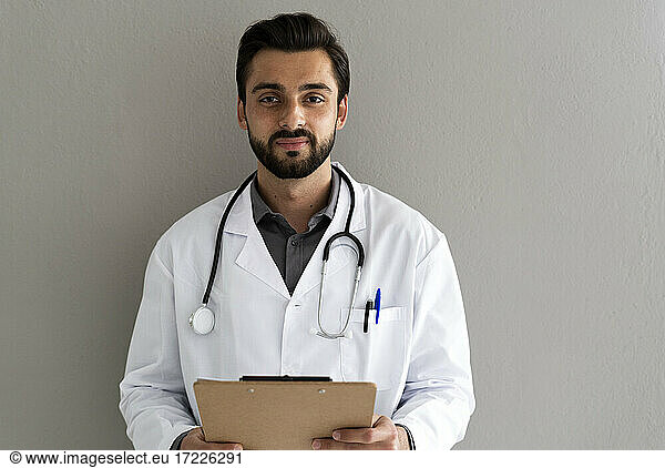 Männlicher Mitarbeiter im Gesundheitswesen mit Stethoskop vor einer Wand stehend