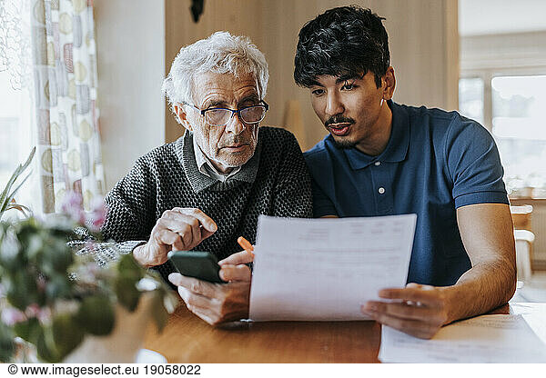 Männlicher Pflegehelfer erklärt einem älteren Mann zu Hause medizinische Berichte