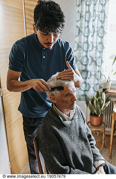 Männlicher Pflegehelfer kämmt das Haar eines älteren Mannes zu Hause