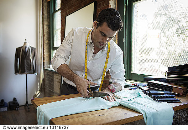 Männlicher Profi schneidet Stoff in der Textilwerkstatt