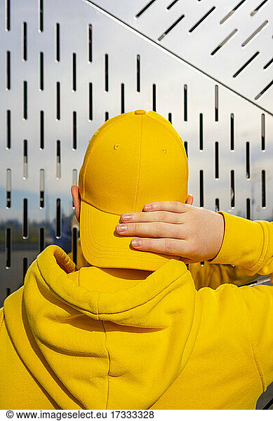 Männlicher Schlittschuhläufer vor der Pubertät  der an einem sonnigen Tag seine gelbe Mütze zurechtrückt