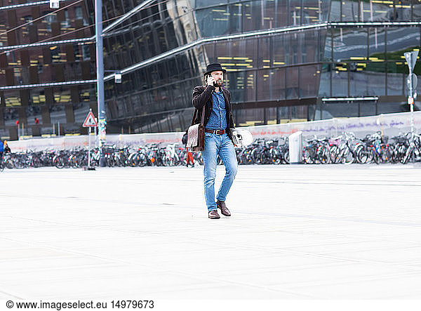 Männlicher Skateboarder schlendert auf dem Stadtplatz und telefoniert mit seinem Smartphone  Freiburg  Baden-Württemberg  Deutschland