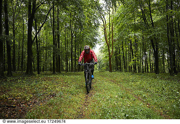 Männlicher Sportler in Sportkleidung beim Fahrradfahren auf einem Waldweg