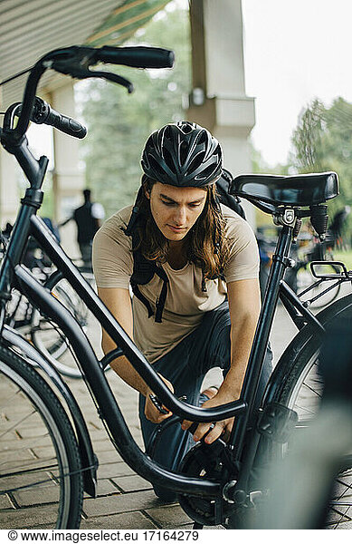 Männlicher Student beim Aufschließen des Fahrrads an einer Parkstation auf dem College-Campus