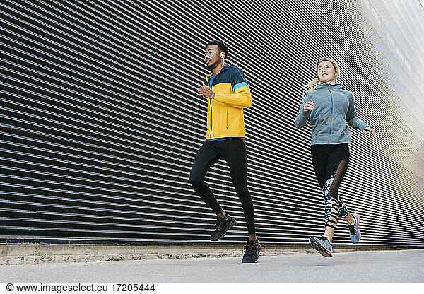 Männlicher und weiblicher Athlet  der beim Sporttraining an der Wand auf dem Gehweg läuft