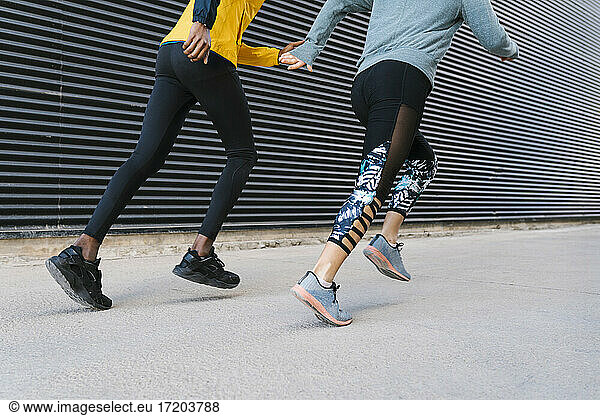 Männlicher und weiblicher Athlet laufen zusammen auf dem Bürgersteig an der Wand