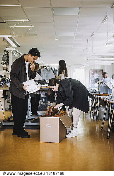 Männlicher und weiblicher Modedesigner beim Auspacken eines Kartons in einer Werkstatt