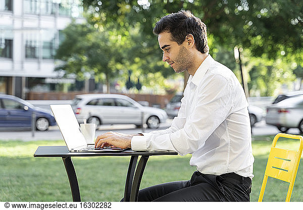 Männlicher Unternehmer arbeitet an einem Laptop auf einem Tisch in einem Straßencafé