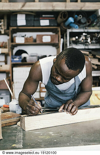 Männlicher Unternehmer  der beim Upcycling in der Werkstatt auf Holz markiert
