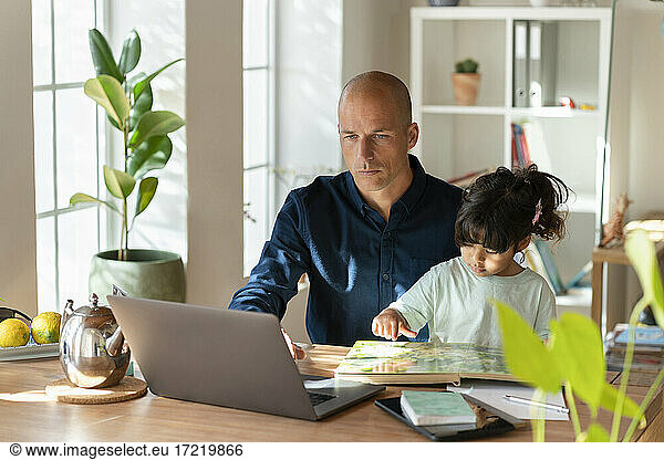 Männlicher Unternehmer  der mit seiner Tochter an einem Laptop arbeitet  während er zu Hause arbeitet
