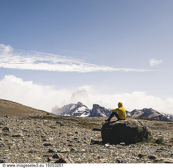 Männlicher Wanderer,  der auf einem Felsen sitzend die Landschaft gegen den Himmel betrachtet,  Patagonien,  Argentinien
