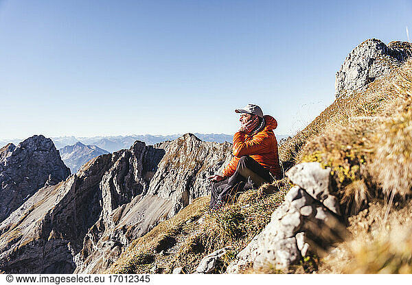 Männlicher Wanderer  der auf einem Berg sitzend gegen den klaren Himmel an einem sonnigen Tag nachdenkt
