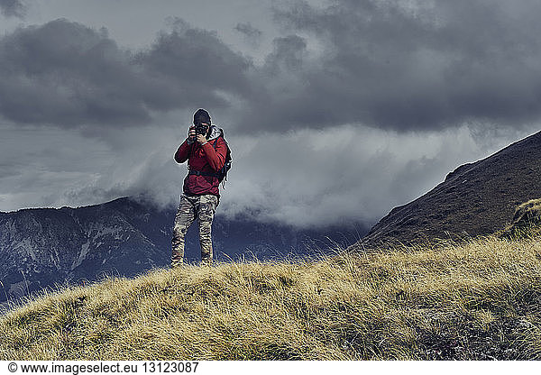Männlicher Wanderer fotografiert im Stehen auf Berg vor bewölktem Himmel