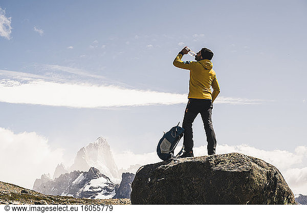 Männlicher Wanderer trinkt Wasser  während er auf einem Felsen gegen den Himmel steht  Patagonien  Argentinien