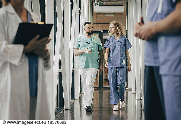 Männliches medizinisches Fachpersonal erklärt einem Kollegen auf dem Flur eines Krankenhauses