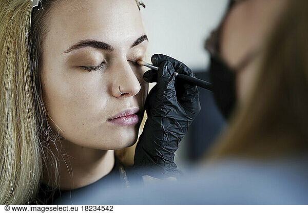 Make-up artist applying eyeshadow on customer's eyelid in salon