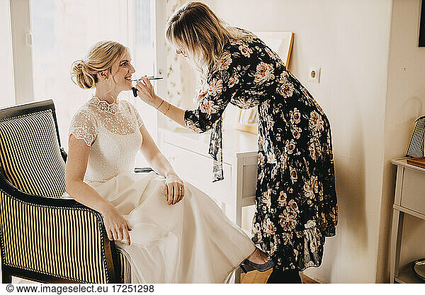 Make-up artist applying lipstick on excited bride during wedding
