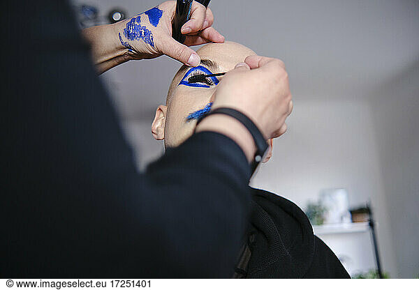 Make-up artist applying mascara on male model's eyelash at studio