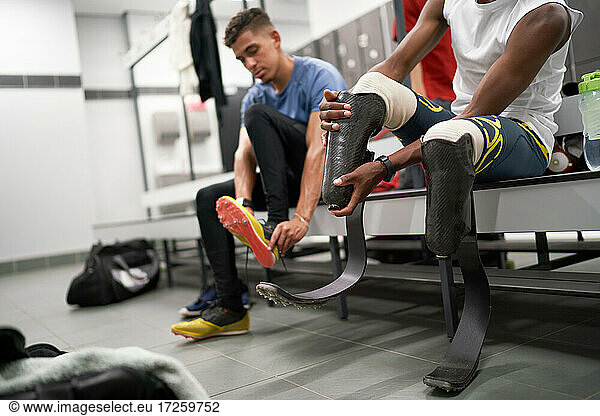Male amputee athlete adjusting running blade prosthetic in locker room