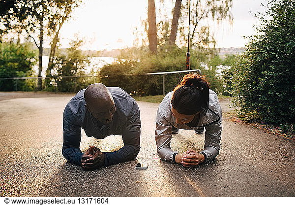 Male and female athletes doing plank exercise on road at park during sunset