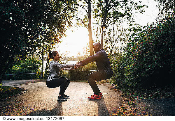 Male and female athletes holding hands while practicing chair position on road in park