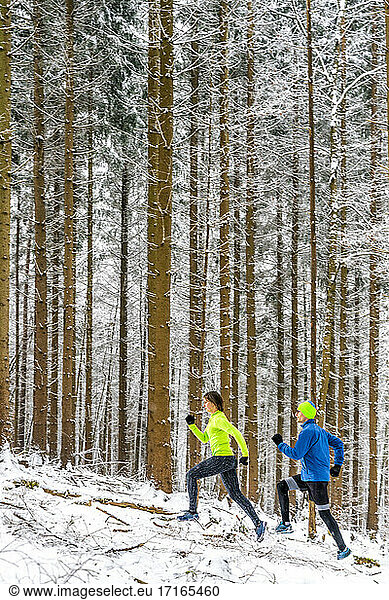 Male and female athletes running on trail in forest during winter