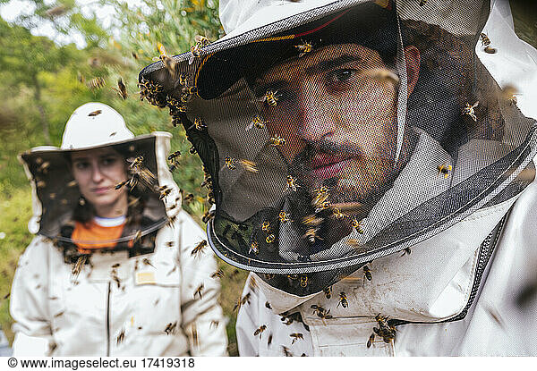 Male and female beekeeper with honey bees on protective suit at farm