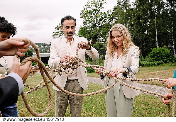 Male and female business professionals holding tangled rope while standing in lawn