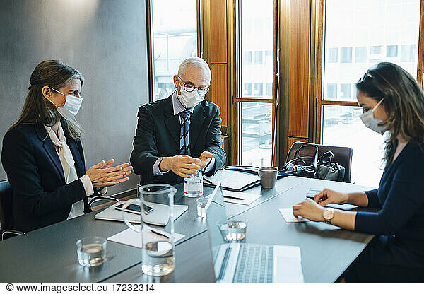 Male and female colleagues applying sanitizer in board room at office during pandemic