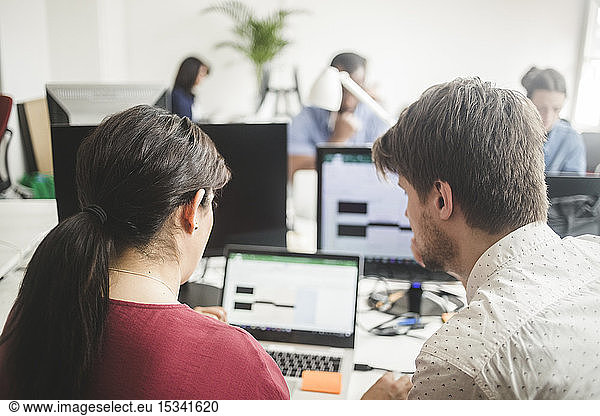 Male and female colleagues discussing over laptop on desk in creative office