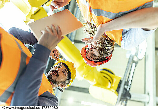 Male and female colleagues discussing robotic machine in industrial factory  low angle view