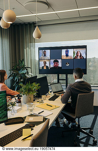 Male and female colleagues looking at TV screen during video conference in coworking office