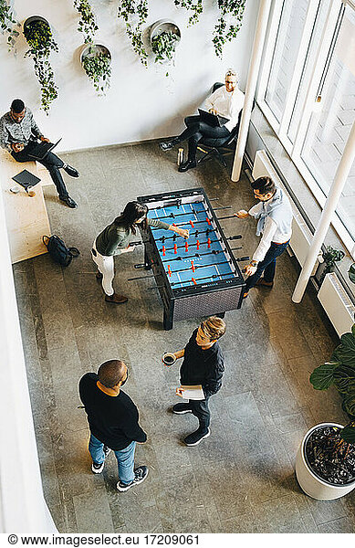 Male and female colleagues playing foosball while taking break from work in office