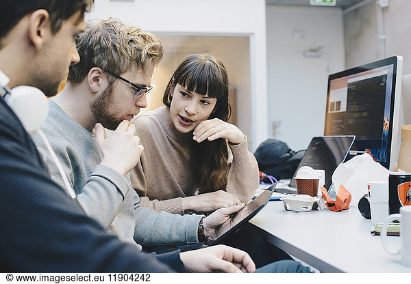 Male and female computer programmers discussing over digital tablet at desk in office
