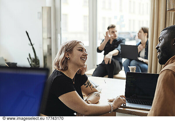 Male and female computer programmers discussing while sitting at tech start-up office