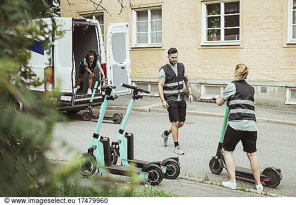 Male and female coworkers loading electric push scooter in delivery van