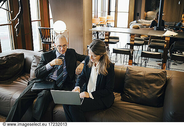Male and female entrepreneur discussing over laptop while having coffee in cafeteria