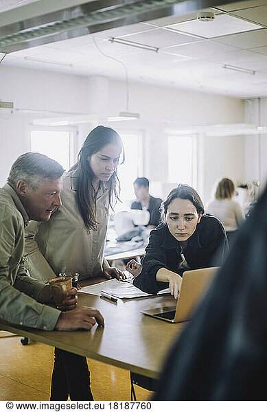 Male and female fashion designers looking at laptop during meeting at workshop