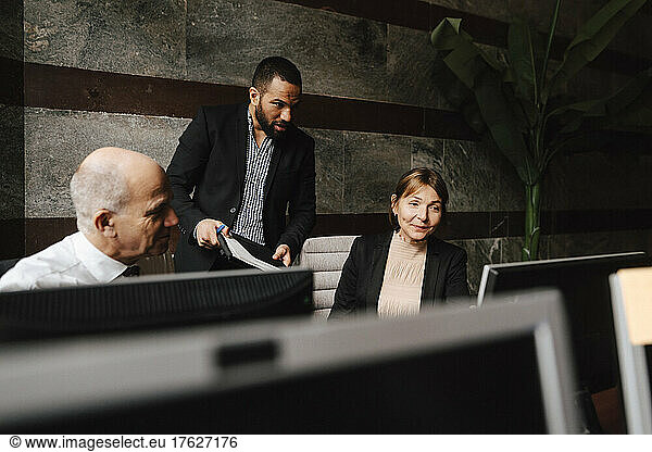 Male and female financial advisors discussing together over computer monitor at workplace