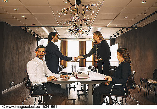 Male and female financial advisors greeting while colleagues sitting at table in law office
