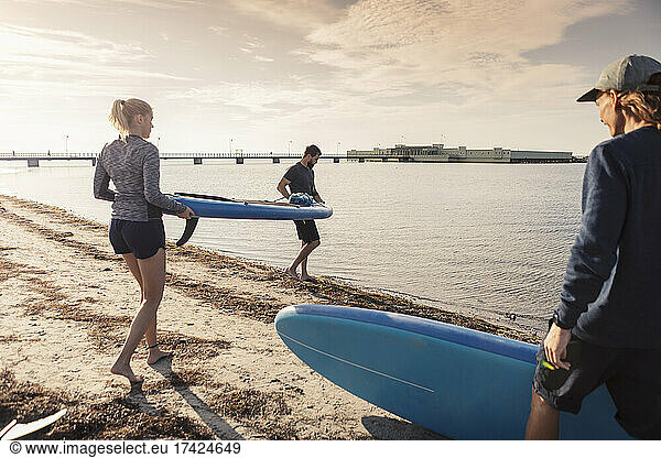 Male and female friends carrying paddleboard at beach