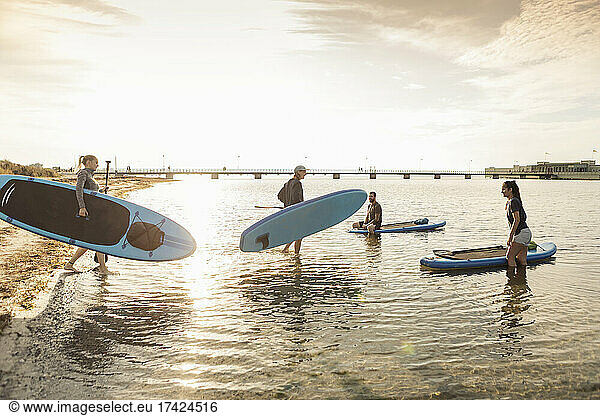 Male and female friends carrying paddleboard in sea