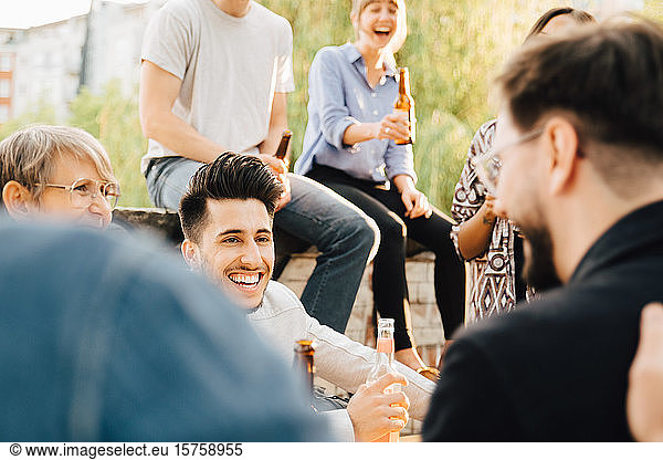 Male and female friends laughing while holding beer at garden party